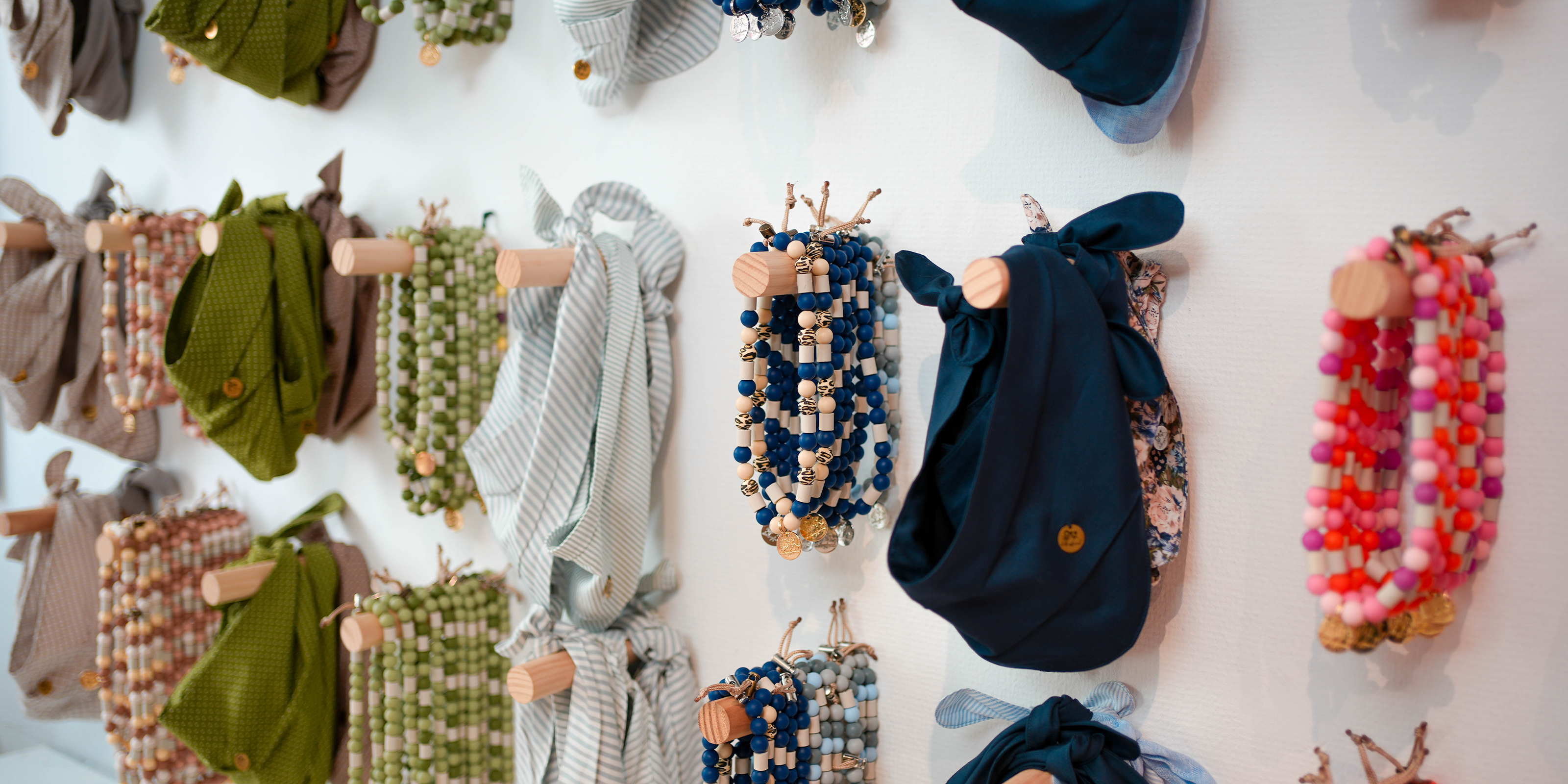 Bunte EM-Keramik-Halsbänder und Hundehalstücher in Blau, Grün und Rosa, liebevoll an Holzhalterungen in der Lieblingsfreund Boutique ausgestellt.