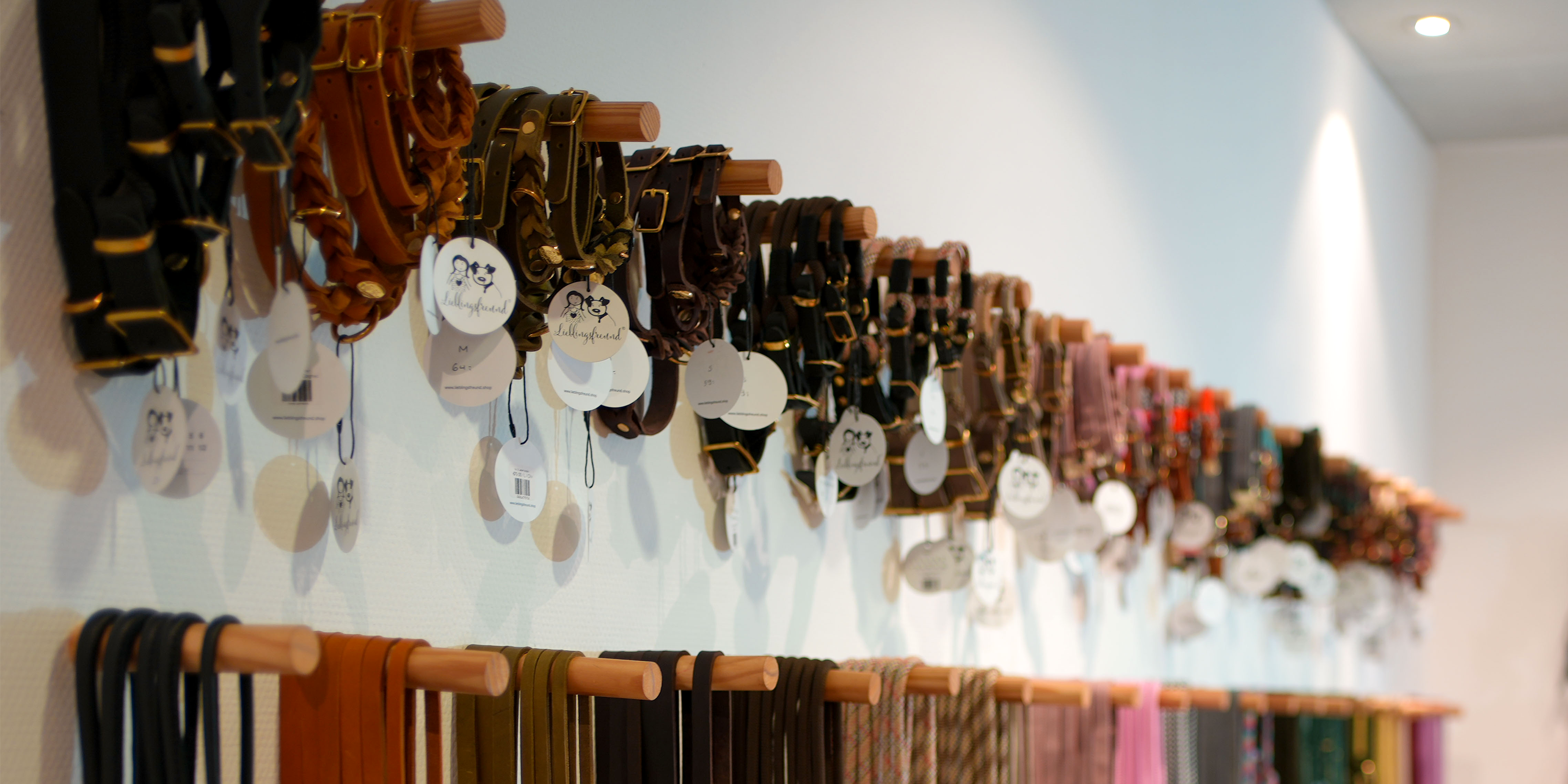 Hochwertige Hundehalsbänder in verschiedenen Farben und Materialien, ordentlich an Holzhalterungen in der Lieblingsfreund Boutique ausgestellt.
