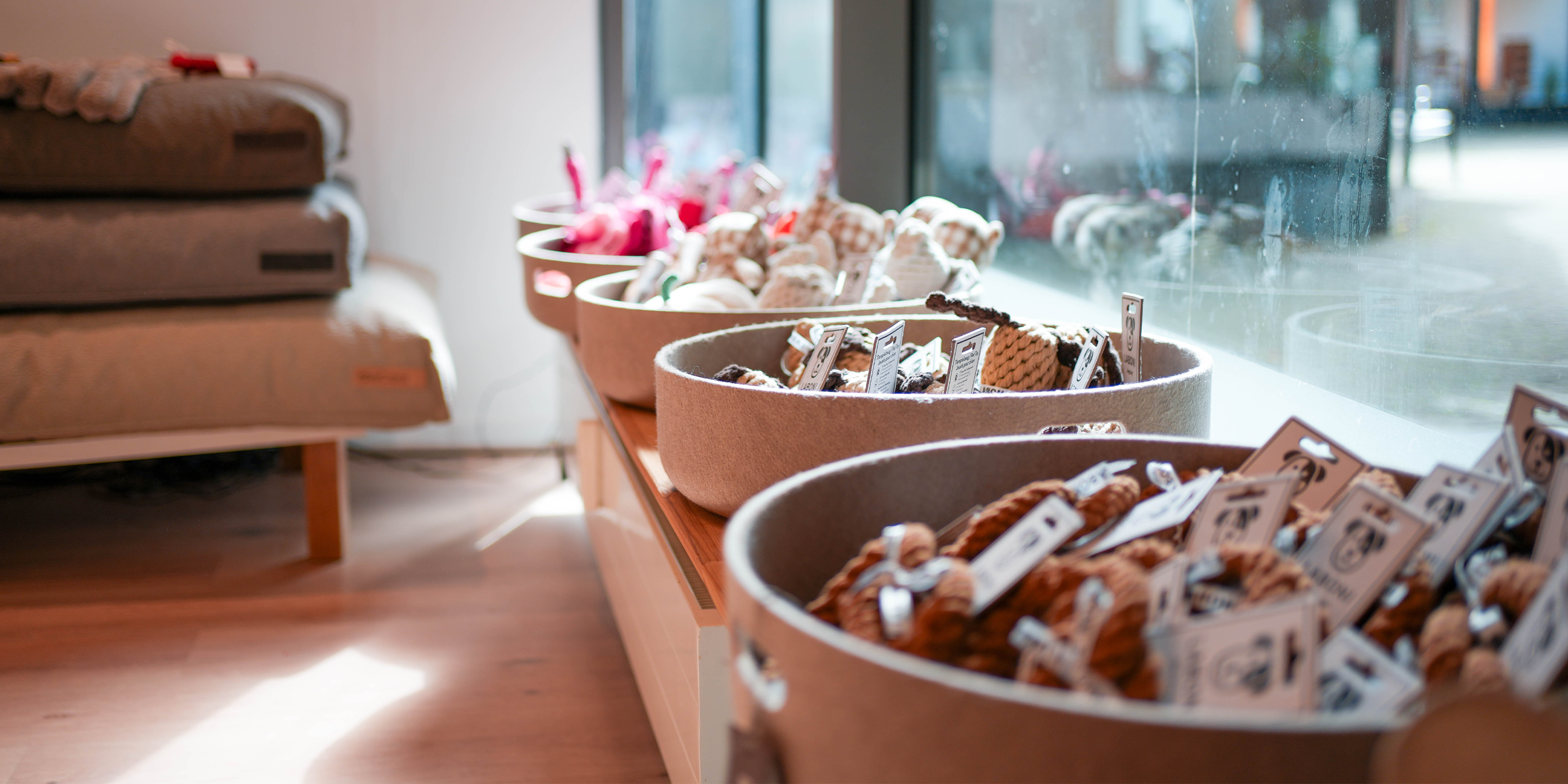 Natürliche Hundespielzeuge aus Stoff und Seil in großen Körben, liebevoll präsentiert am Fenster der Lieblingsfreund Boutique.